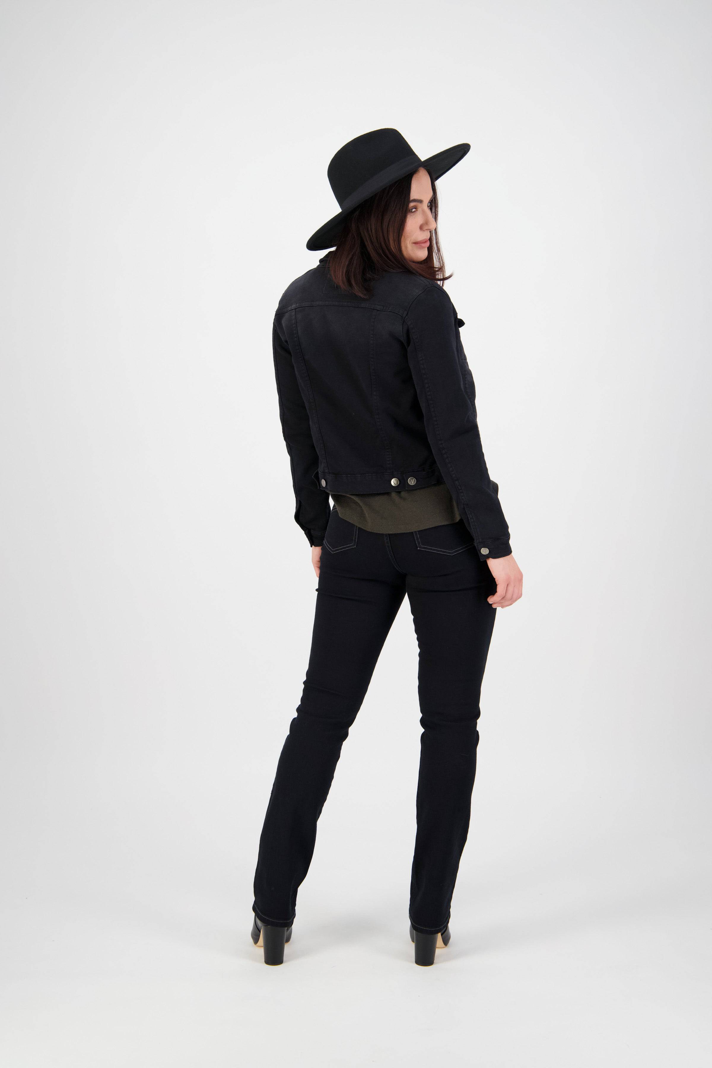A woman in a black hat, black pants, and the Vassalli Rider Knit Jacket - Black stands with her back to the camera, head turned to the side, against a plain white background.
