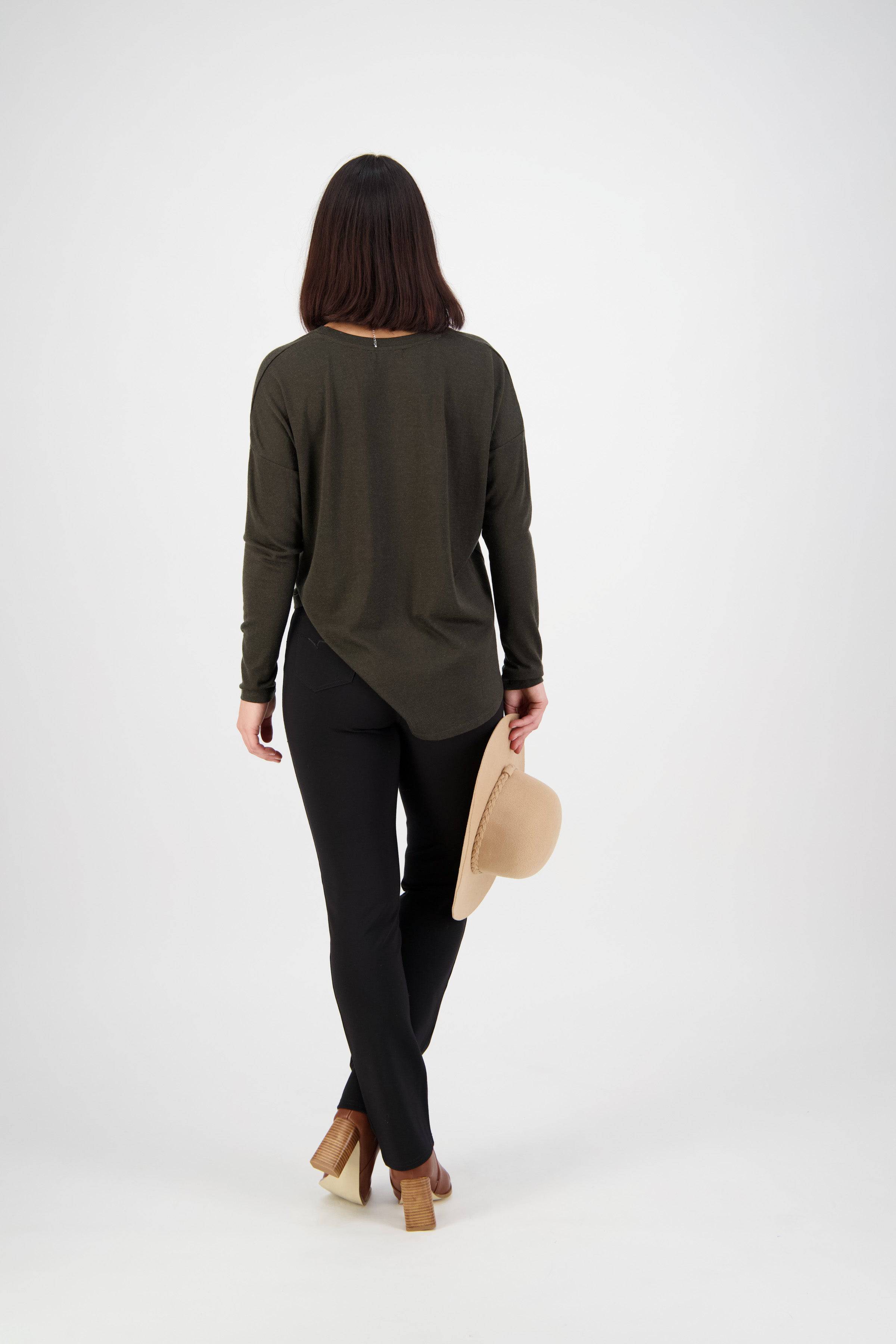 A woman with brown hair faces away against a white background, wearing a dark green long-sleeve top, Vassalli Bay Ponti Pull On - Black pants, tan heeled shoes, and holding a beige hat in her left hand.