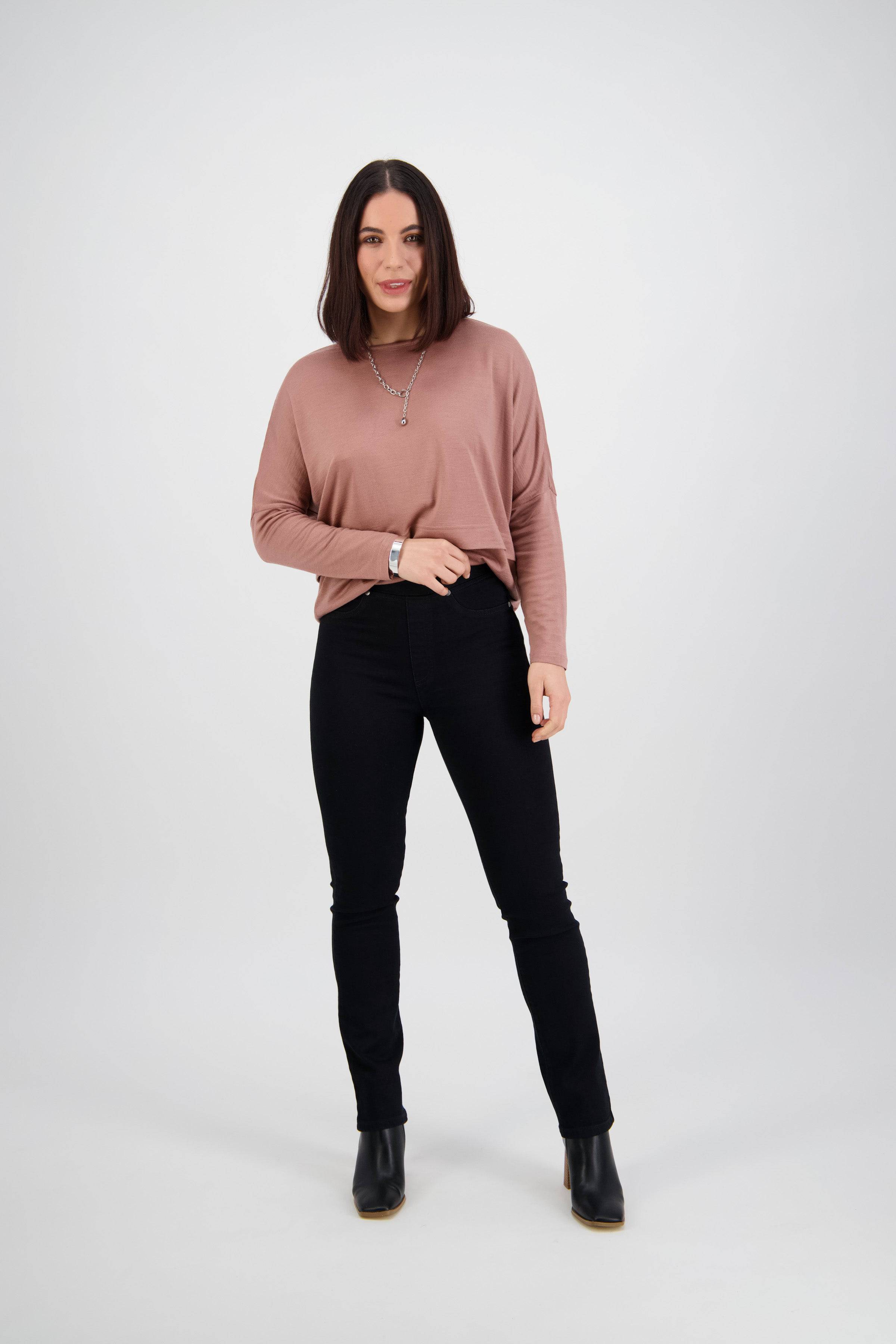A woman with straight, shoulder-length brown hair faces forward, wearing a mauve long-sleeve top, Vassalli's Bay Pull On - Black Denim pants, and black ankle boots against a plain light background.