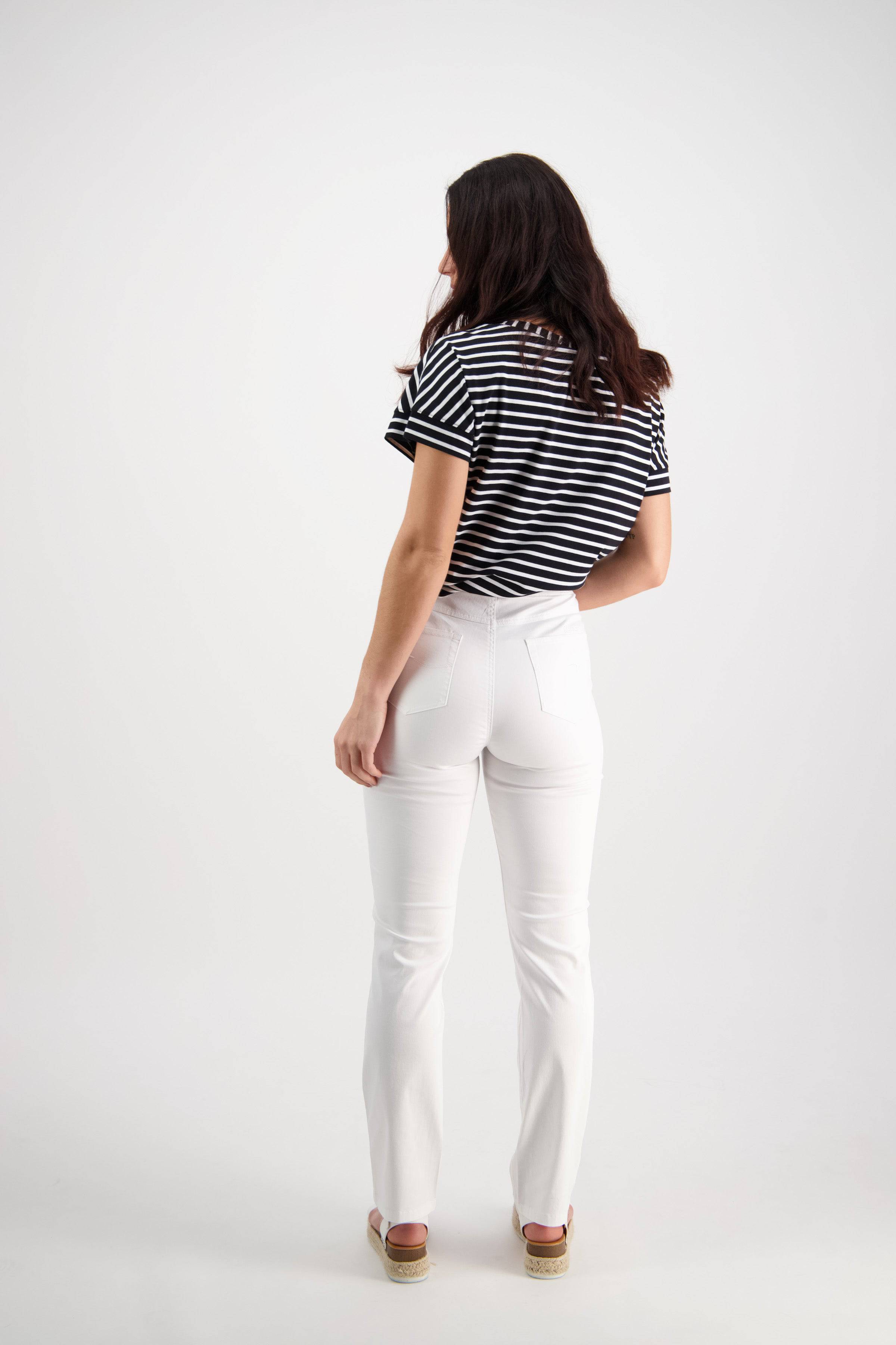 A woman with long dark hair faces away, wearing a black and white striped shirt and Vassalli Bay Pull On - White slim leg pants with sandals, set against a plain white background.