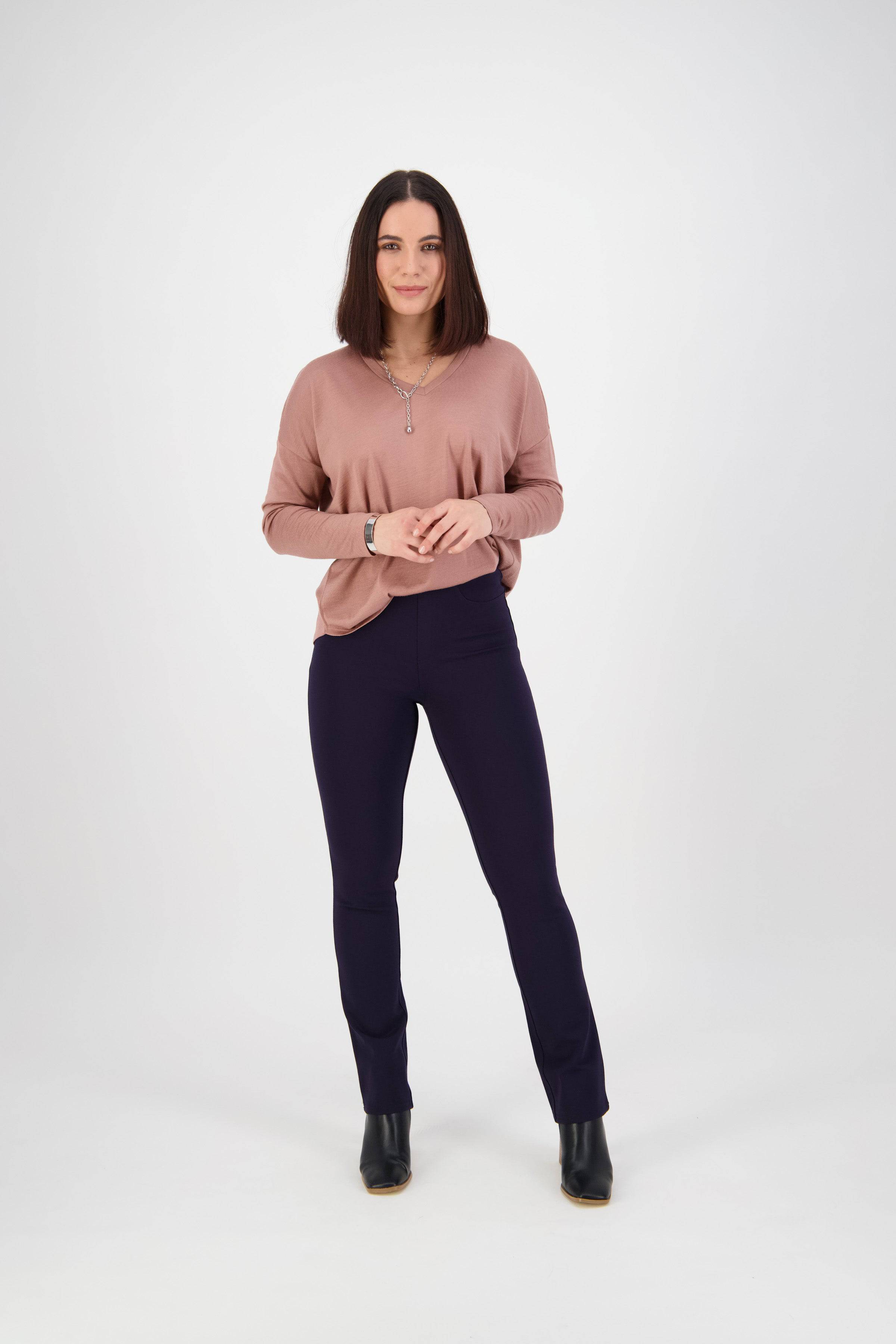 A woman with straight, shoulder-length dark hair stands facing forward, wearing a mauve long-sleeve top, Vassalli Bay Ponti Pull On pants in navy, and black boots against a plain white background.