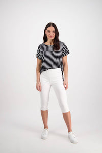 A woman with long brown hair stands confidently against a white background, wearing Vassalli's Atlas 3/4 Pant in white, a black and white striped top, and white sneakers.