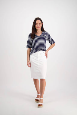 A woman with long, straight hair and a confident look wears the Vassalli Poppy Poplin Skirt in white, styled with a navy-and-white striped short-sleeve top and white platform sandals against a plain background.