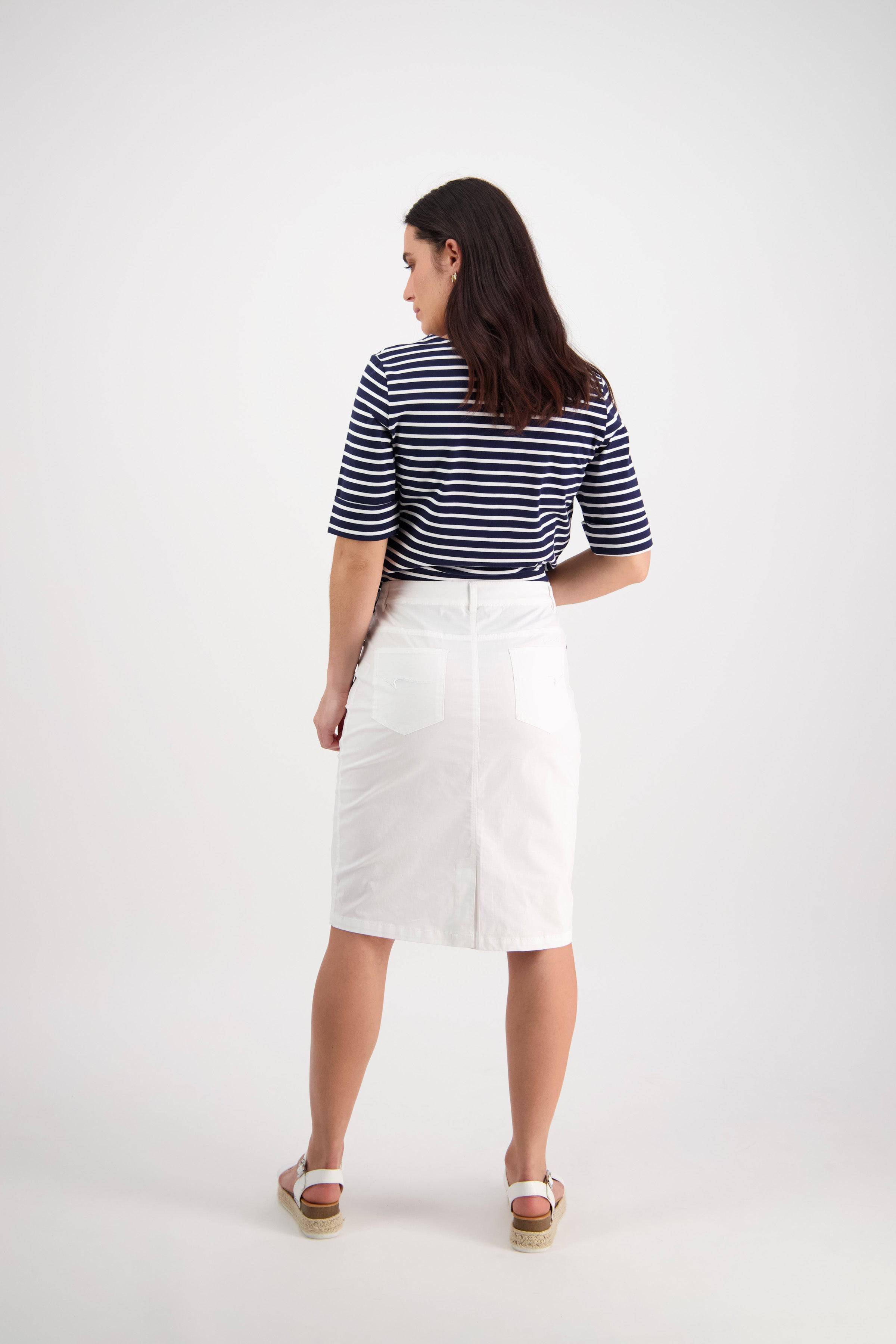 A woman faces away, wearing a navy and white striped shirt, the Vassalli Poppy Poplin Skirt in white, and white sandals. Set against a light background, this look is perfect for effortless everyday style.