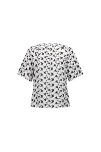 The Vassalli V-Neck Top - Floral is a short-sleeved, loose-fit white blouse with an all-over black abstract print, shown from the back on a plain white background.