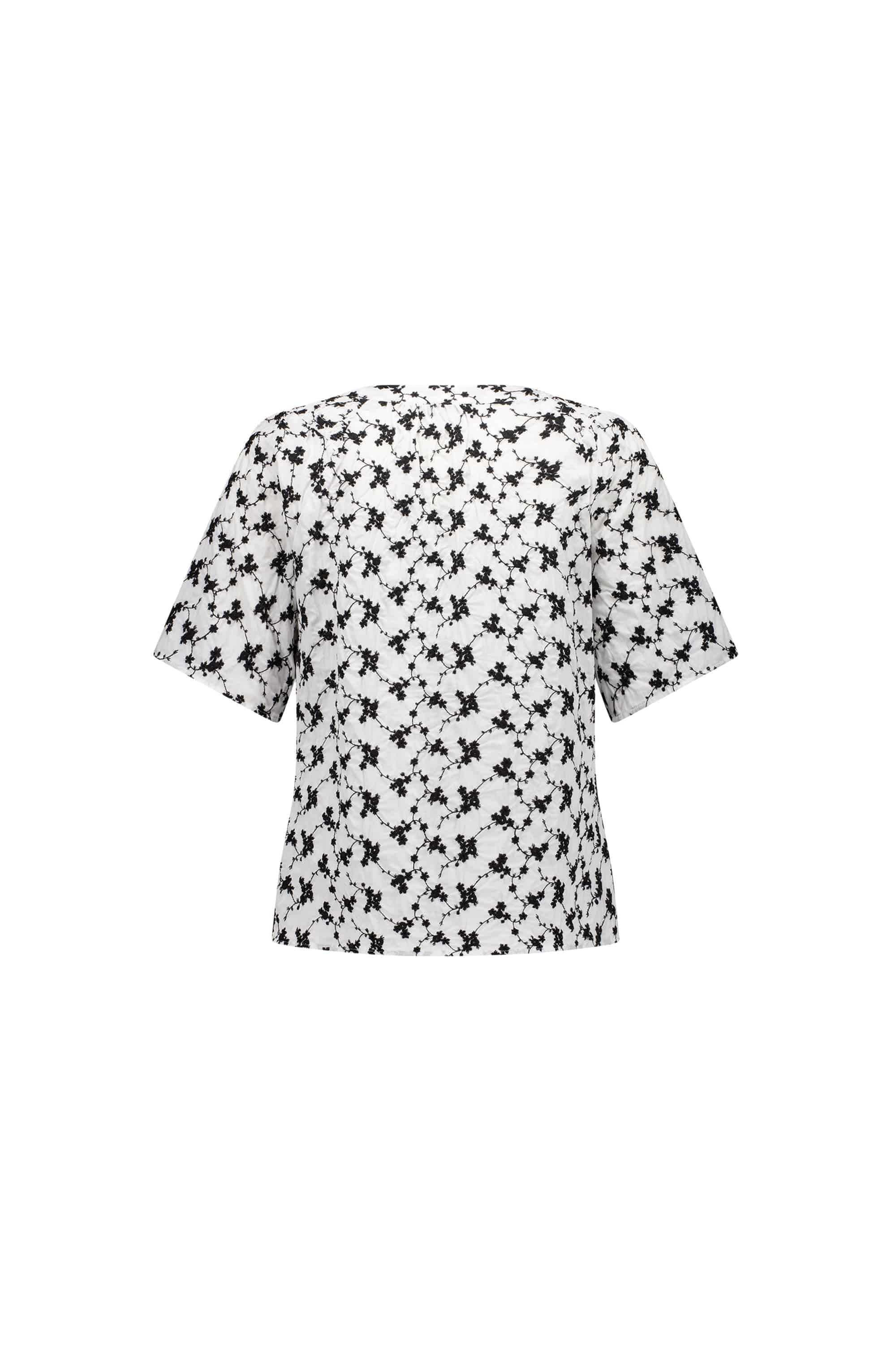 The Vassalli V-Neck Top - Floral is a short-sleeved, loose-fit white blouse with an all-over black abstract print, shown from the back on a plain white background.