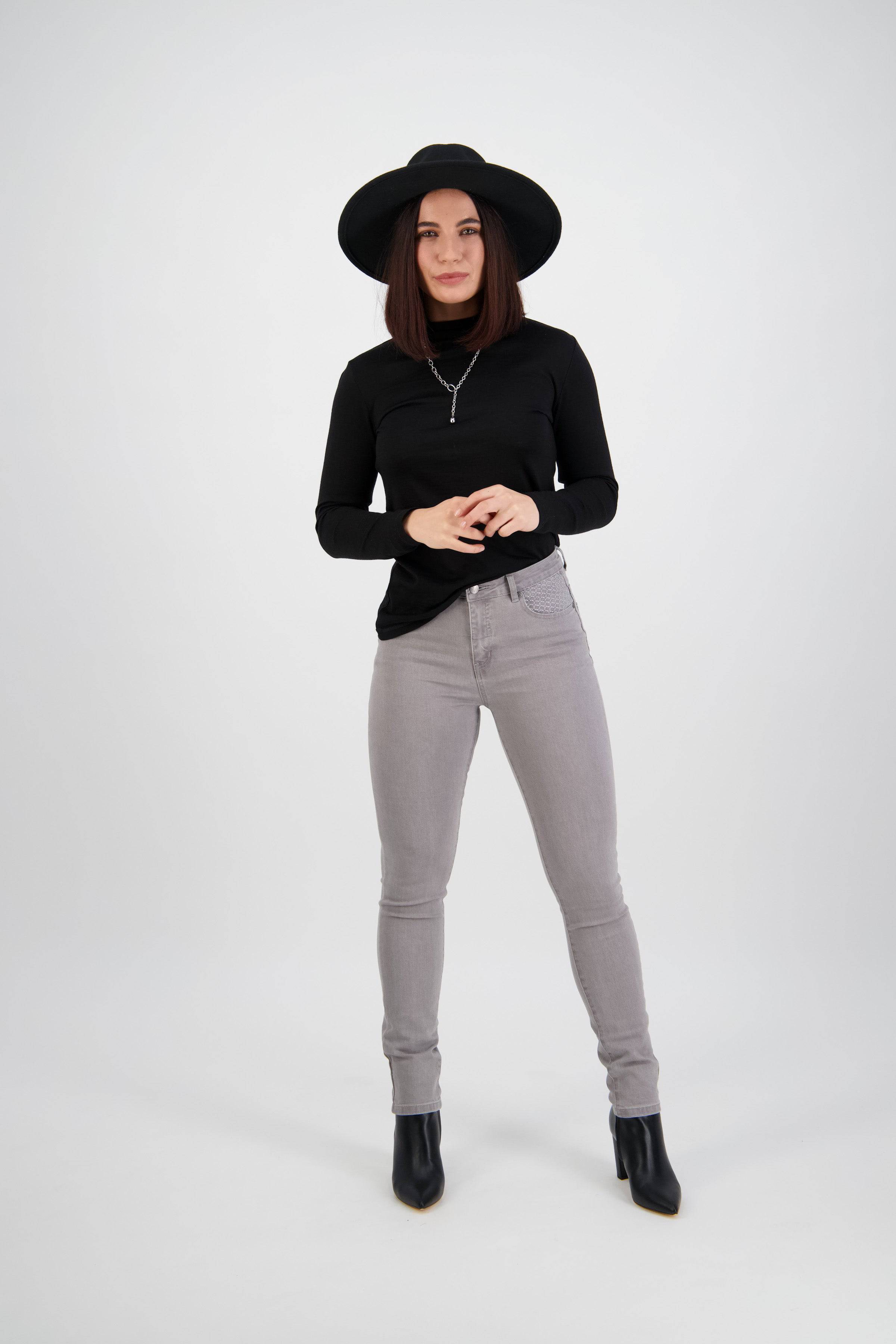 A woman in a black wide-brimmed hat, black long-sleeve top, Vassalli Reign Jean - Light Grey, and black ankle boots stands against a white background, looking forward with her hands loosely clasped.