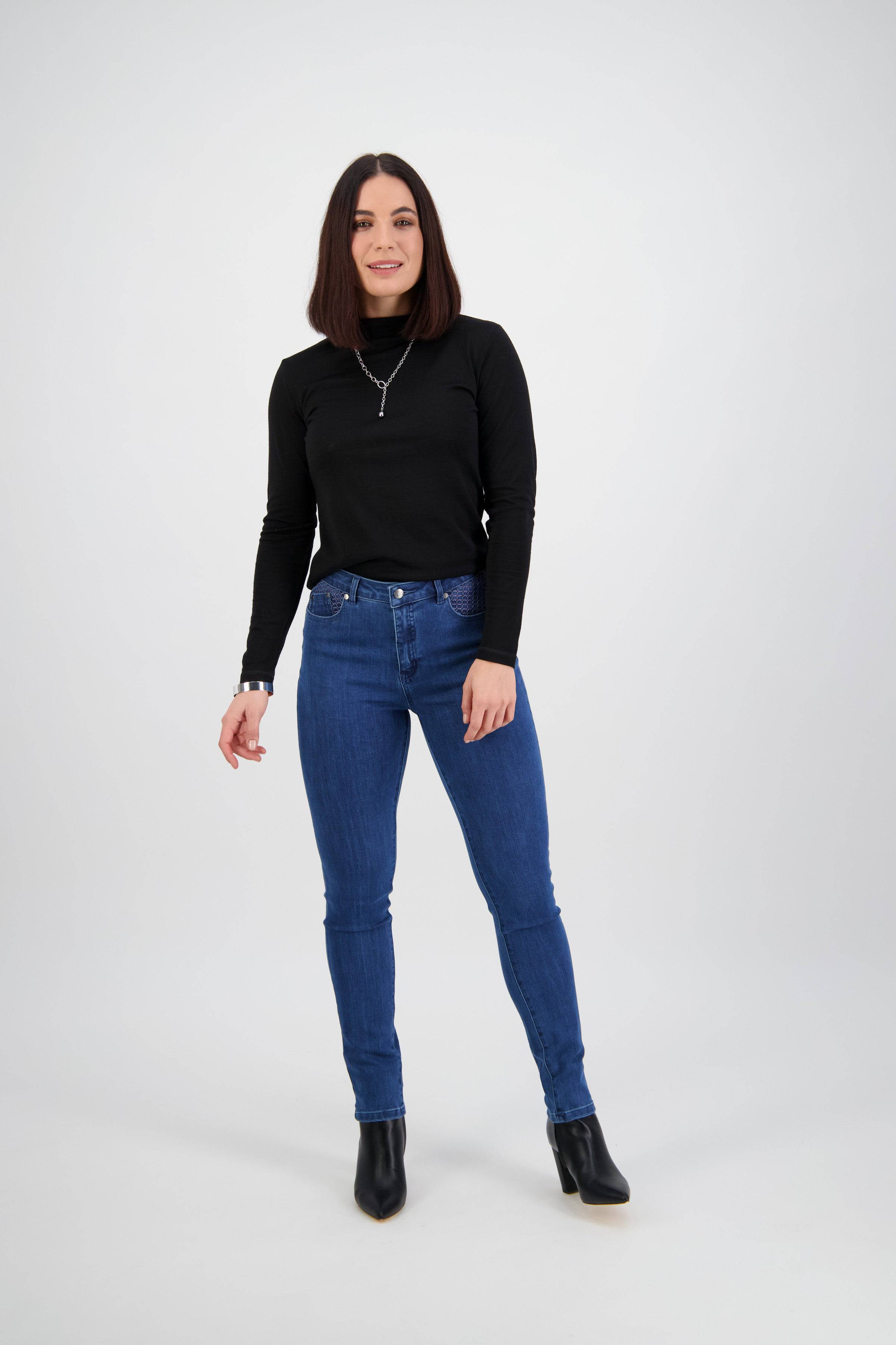 A woman with shoulder-length dark hair wears the Vassalli Reign Jean - Plain New Blue, paired with a black long-sleeve top and black ankle boots. She faces the camera, smiling slightly, against a plain light background.