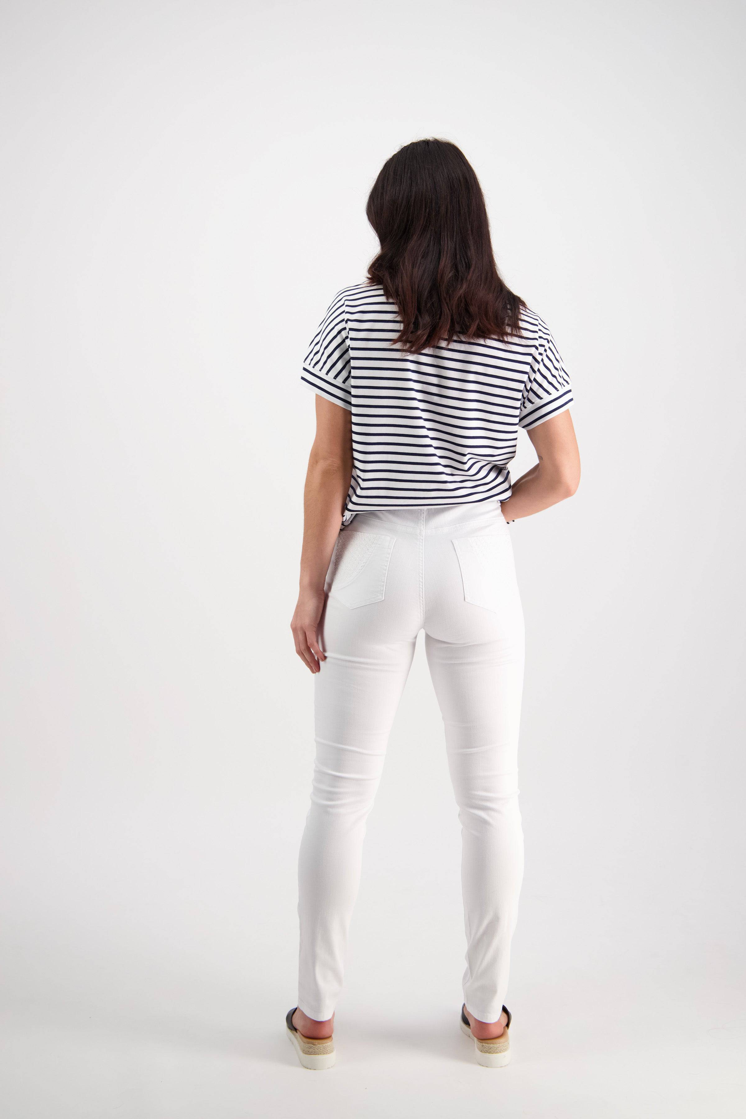 A woman with dark hair faces away from the camera, wearing a black and white striped short-sleeve shirt and Vassalli Reign Jean in white denim, paired with beige shoes, against a plain white background.