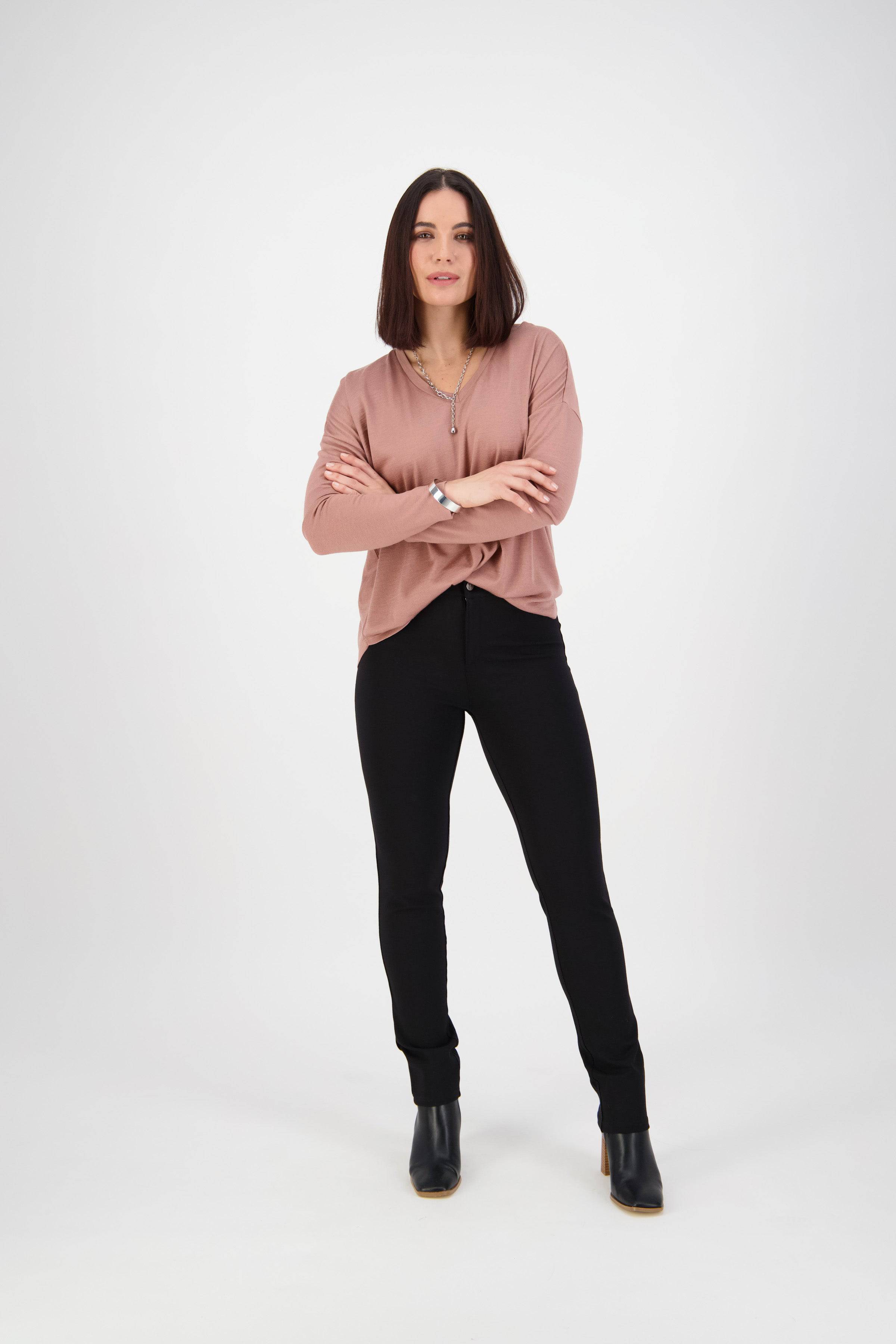 A woman with straight, shoulder-length brown hair stands with arms crossed, wearing a mauve long-sleeve top and Vassalli Ponti Pant - Black, paired with black heeled boots against a plain white background.