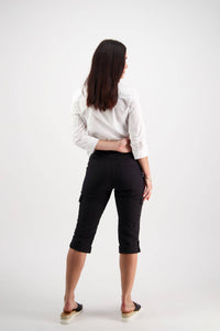 A woman with straight brown hair, wearing a white shirt and Vassalli Wave Pant - Black, featuring an adjustable waistband, stands facing away with one hand on her back against a plain white background.