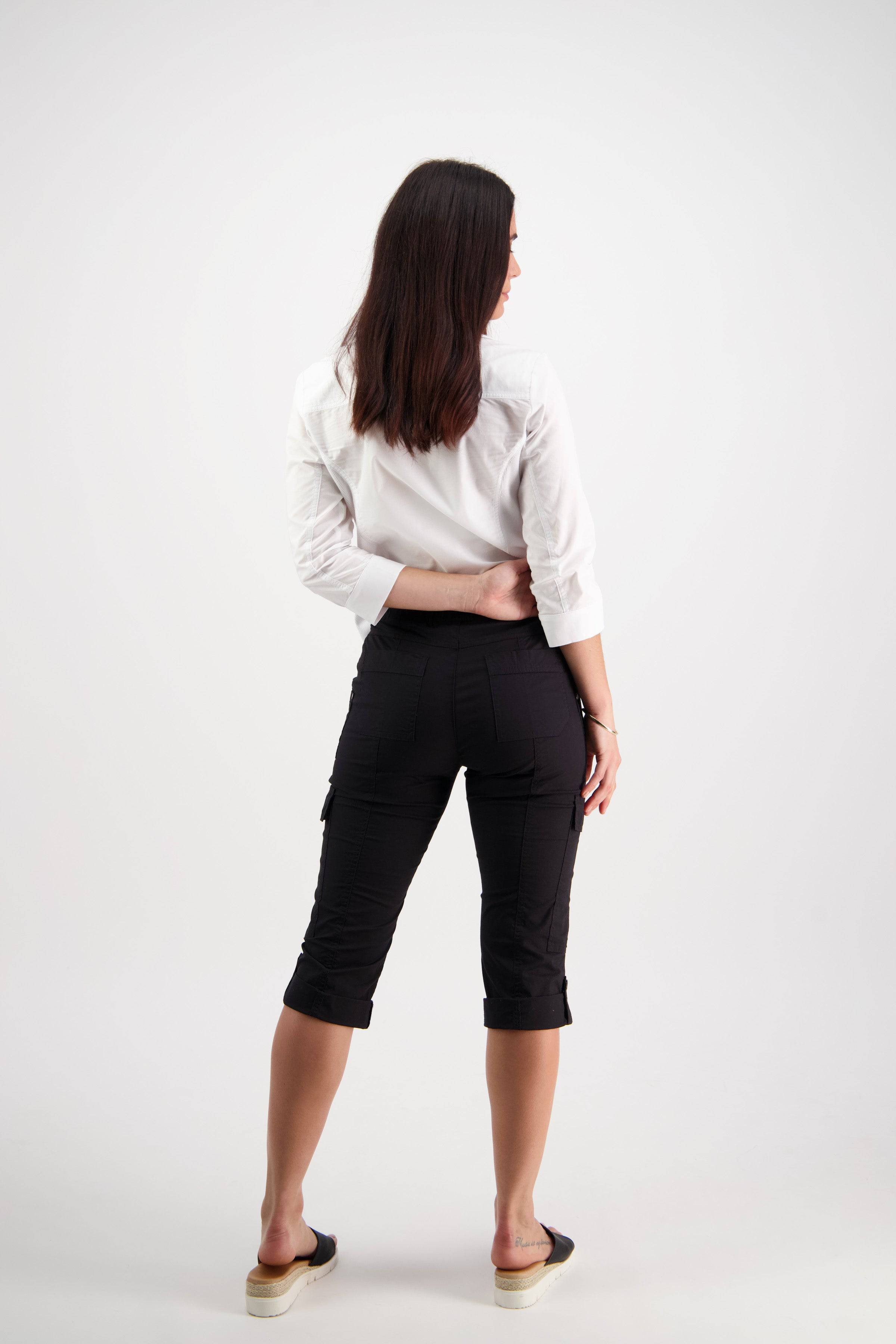 A woman with straight brown hair, wearing a white shirt and Vassalli Wave Pant - Black, featuring an adjustable waistband, stands facing away with one hand on her back against a plain white background.