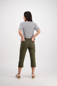 A woman faces away with hands on hips, wearing a black-and-white striped top and Vassalli Wave Pant - Khaki, featuring an adjustable waistband, paired with white sandals against a plain white background.