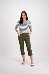 A woman with long dark hair stands confidently against a white background wearing Vassalli's Wave Pant - Khaki, relaxed cargo pants in stretch poplin with an adjustable waistband. She pairs them with a black-and-white striped top and has her hands in her pockets.