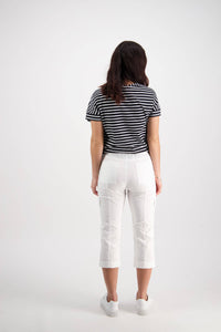 A woman with long dark hair wears a black and white striped short-sleeve shirt, Vassalli Wave Pant - White, and white shoes, standing facing away from the camera against a plain light background.