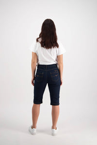 A person with long brown hair, wearing a white t-shirt, Vassalli Alfa Short - Indigo Denim (Contrast Stitch), and white sneakers, stands facing away from the camera against a plain white background.