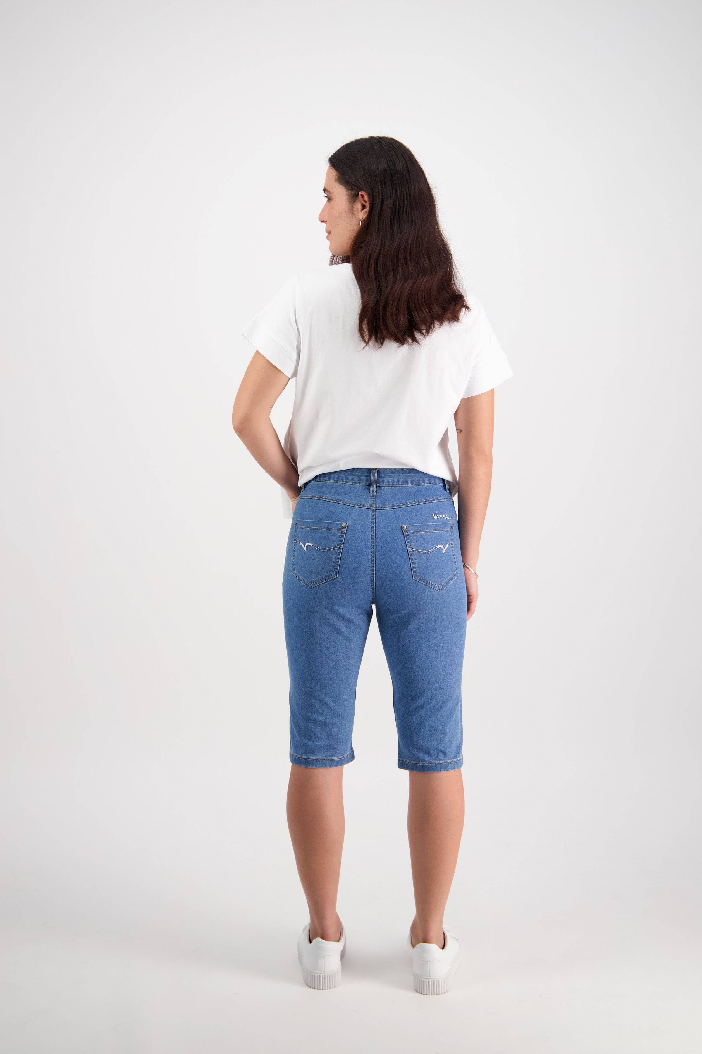 A person stands with their back to the camera, wearing a white t-shirt, Vassalli's Alfa Short - Light Denim (Contrast Stitch) made from stretch denim, and white sneakers against a plain white background.