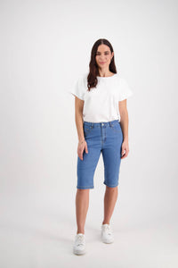 A woman with long brown hair stands against a white background, wearing a white tee, Vassalli’s Alfa Short - Light Denim (Contrast Stitch), and white sneakers. She has a neutral expression, arms relaxed by her sides.