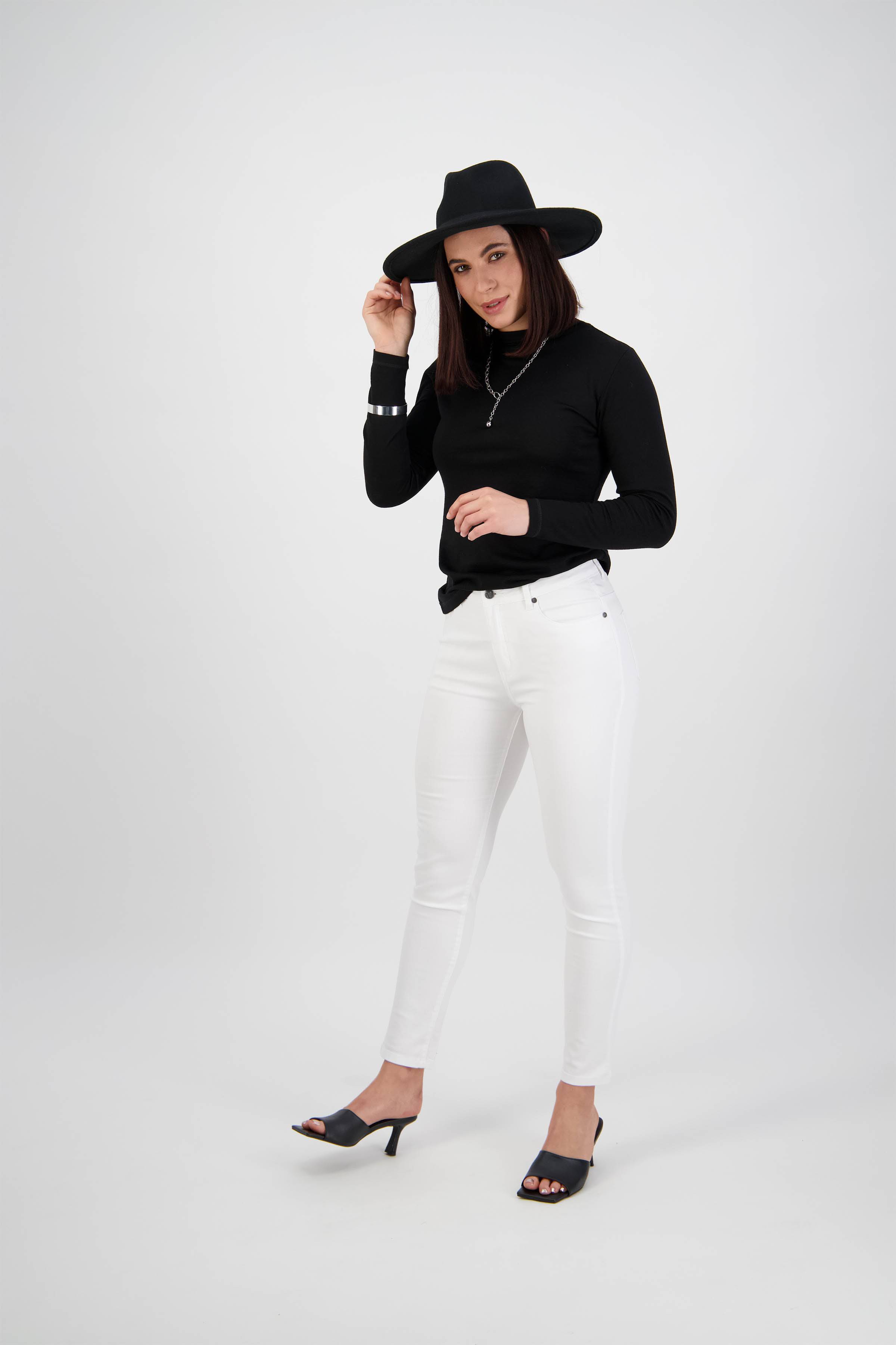 A woman wearing a black wide-brim hat, black long-sleeve top, Vassalli Tide Jean in white denim, and black heeled sandals poses confidently against a plain white background.
