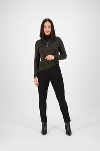 A woman with straight, shoulder-length brown hair stands in a studio against a white background, wearing a dark green long-sleeve turtleneck, Vassalli’s Style Pant - Black, black ankle boots, and a necklace, smiling slightly.