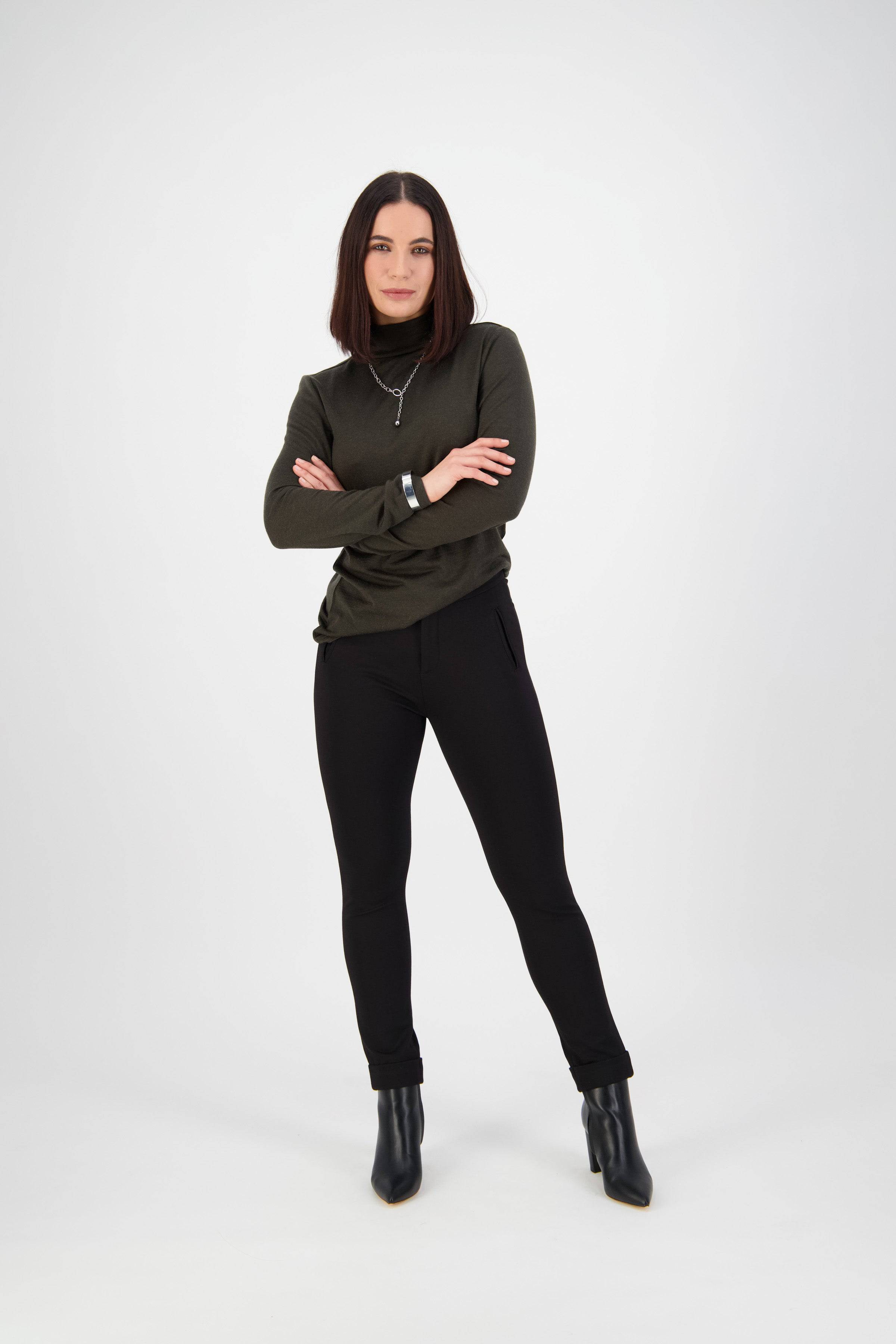 A woman with straight, shoulder-length dark hair poses confidently in a dark green long-sleeve top and Vassalli Style Pant - Black, made from stretch fabric, paired with black ankle boots against a plain white background.