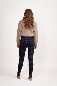 A person with long, wavy brown hair faces away from the camera, wearing a beige textured sweater and Vassalli View Pant - Navy with brown heeled ankle boots, against a white background.