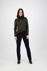 A woman with straight dark hair faces forward in a dark green turtleneck, Vassalli Tour Jean - Black Denim, black boots, and a silver necklace against a plain white background.