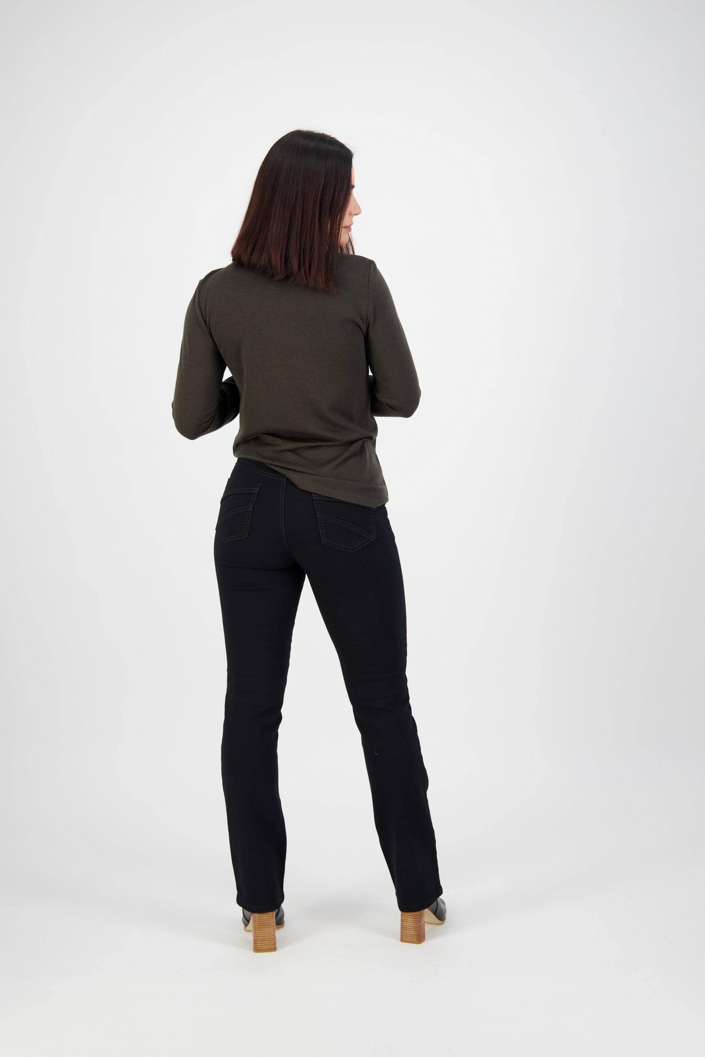 A person with shoulder-length dark hair, wearing a dark green long-sleeve shirt, Vassalli Tour Jean - Black Denim, and heeled shoes stands facing away from the camera against a plain white background.