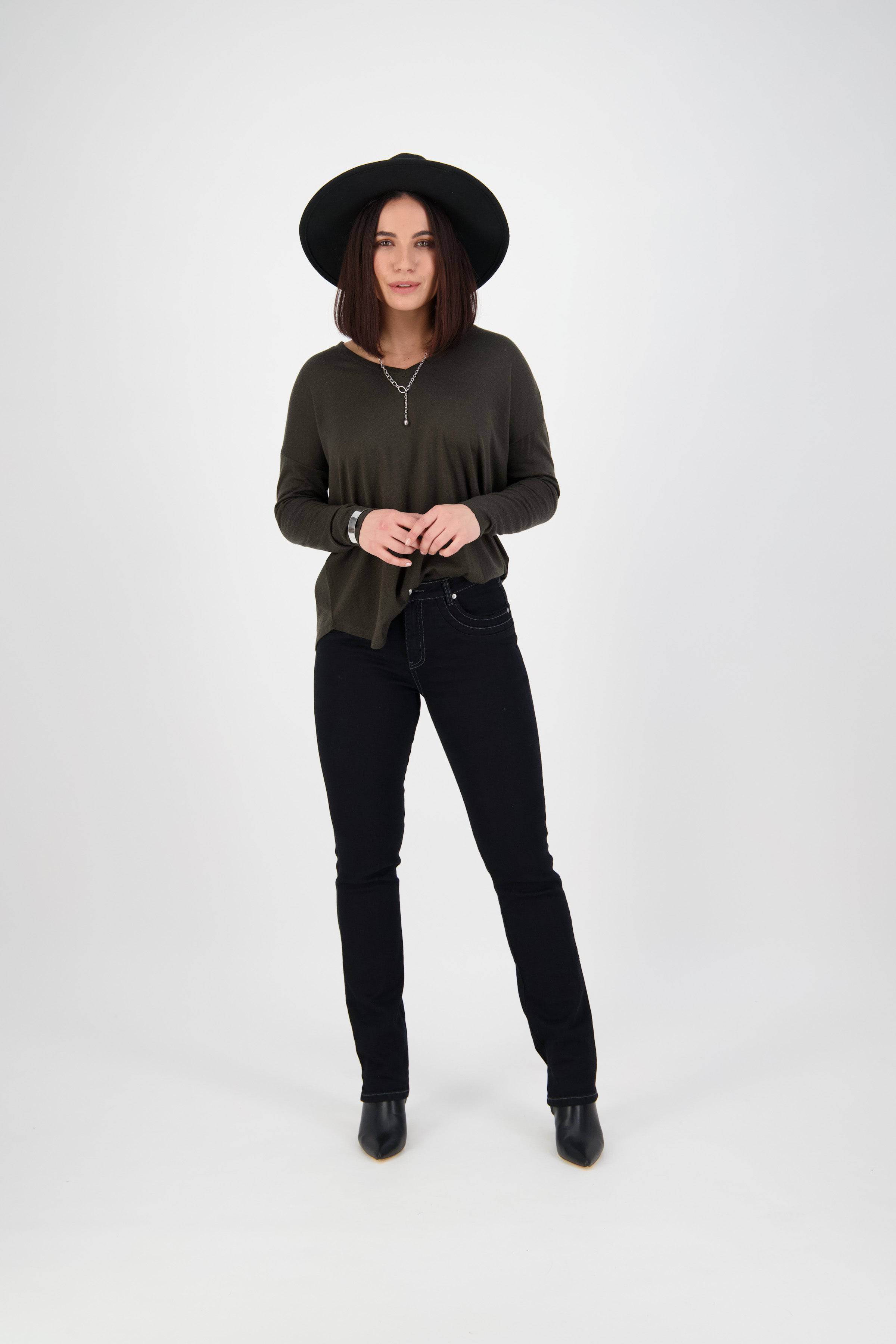 Woman wearing a wide-brimmed black hat, dark green long-sleeve top, Vassalli Studio Jean - Black Denim, and black ankle boots stands against a plain white background.