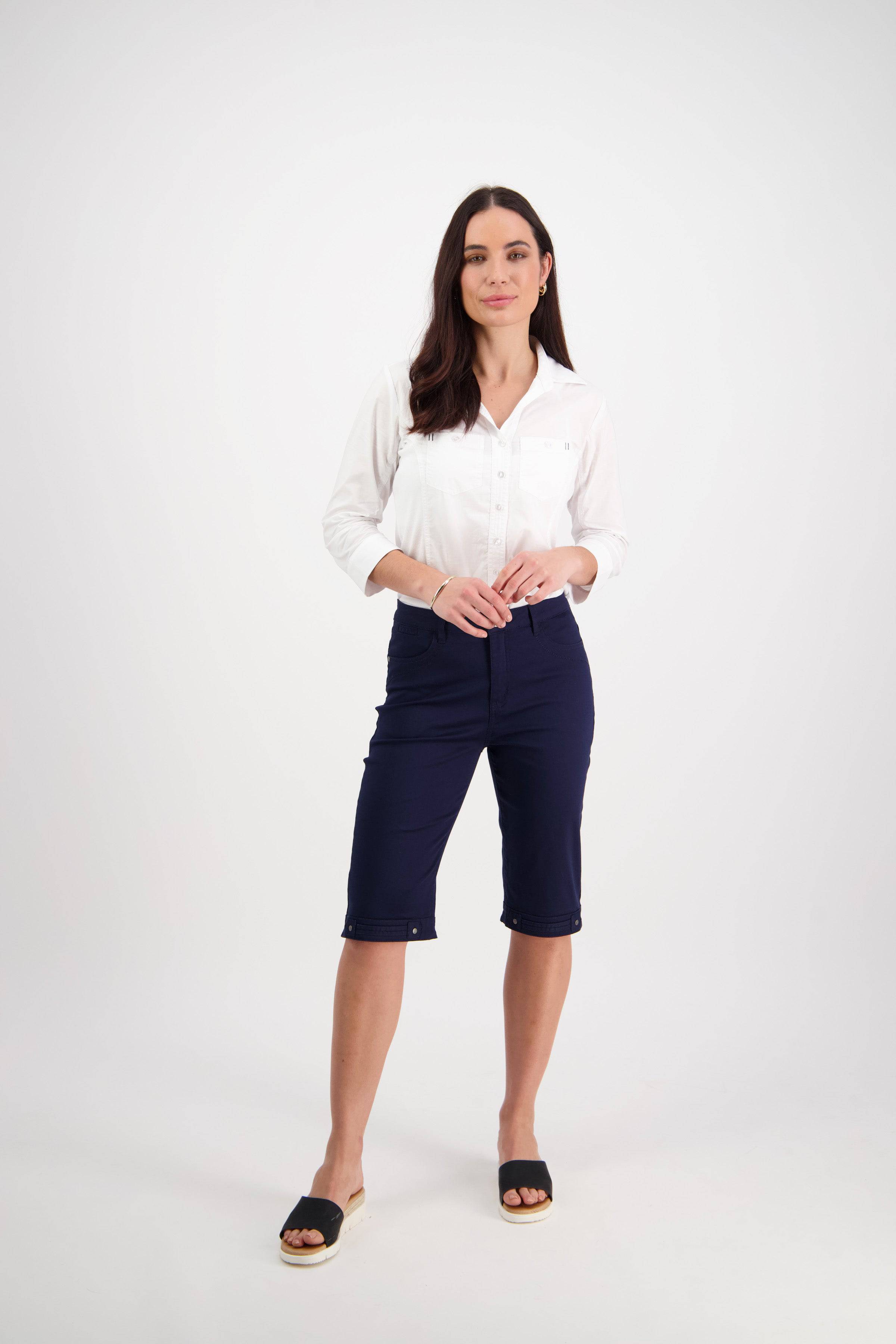 A woman with long brown hair and a neutral expression models the Vassalli Custom Lightweight Short in navy, paired with a white button-up shirt and black slip-on sandals against a plain white background—ideal for summer.