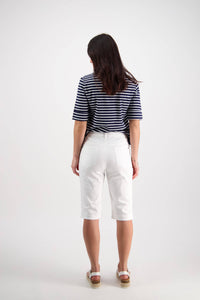 A woman stands facing away in a navy and white striped short-sleeve shirt, Vassalli Custom Lightweight Short in white for comfort, and wedge sandals against a plain white background.