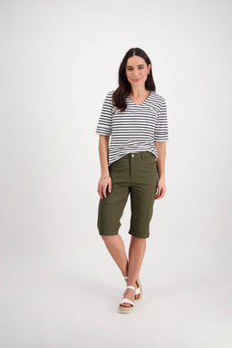 A woman with long dark hair stands against a white background wearing a black-and-white striped short-sleeve shirt, Vassalli Custom Poplin Short in khaki, and white sandals for a relaxed, versatile look.