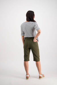 A woman faces away, wearing a black and white striped shirt, Vassalli’s Custom Poplin Short in khaki, and white sandals against a plain light background.