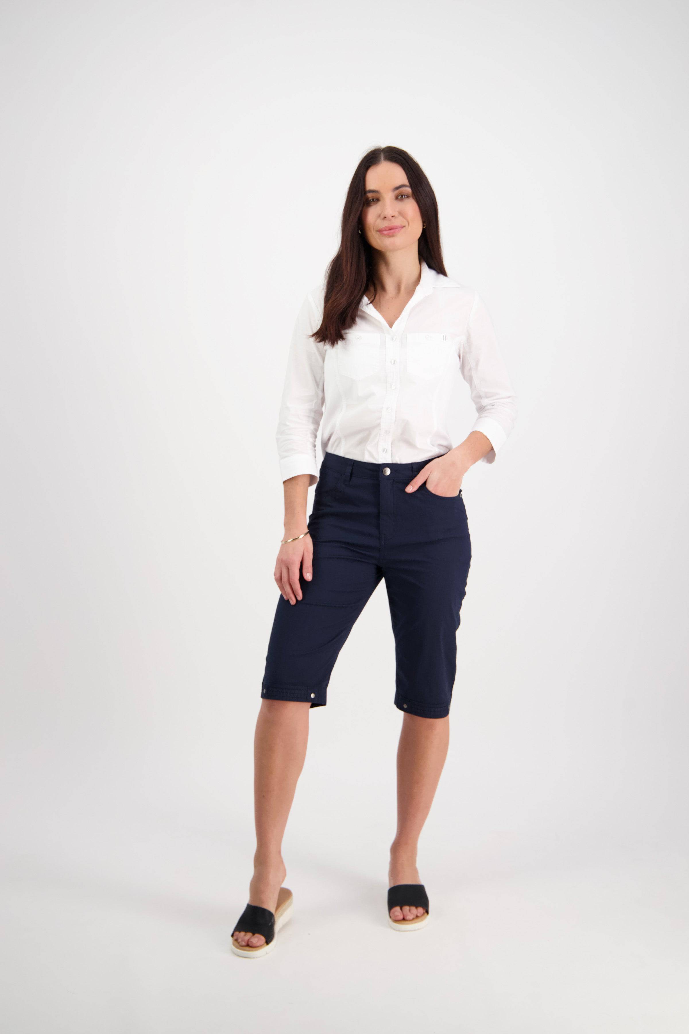 A woman smiles slightly against a white background, wearing the Vassalli Custom Poplin Short in navy—a tailored design with cuffed hems, crafted from lightweight stretch poplin. One hand is in her pocket.