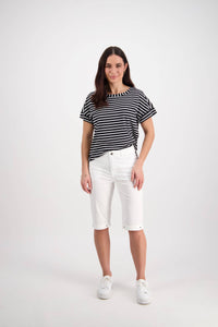 A woman with long brown hair poses casually against a white background, wearing Vassalli's Custom Poplin Short in white, a black and white striped t-shirt, and white sneakers.