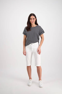A woman with long brown hair poses casually against a white background, wearing Vassalli's Custom Poplin Short in white, a black and white striped t-shirt, and white sneakers.