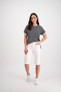 A woman with long brown hair smiles with one hand in her pocket, wearing Vassalli’s Custom Poplin Short in White, a black and white striped short-sleeve top, and white sneakers against a plain white background.