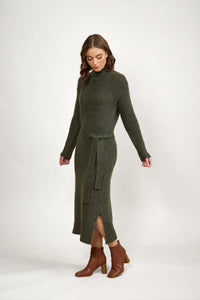 Woman wearing a dark green knit midi dress with long sleeves, waist tie, and brown ankle boots