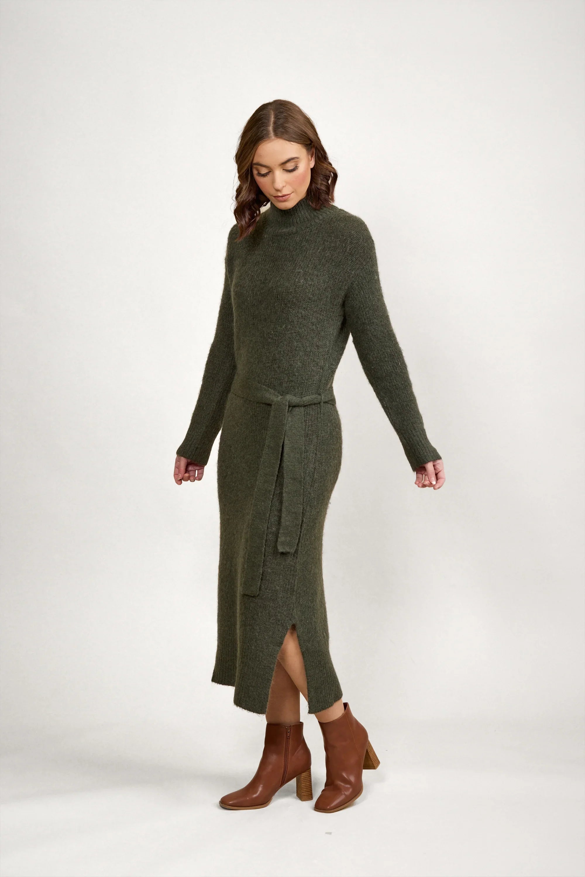 Woman wearing a dark green knit midi dress with long sleeves, waist tie, and brown ankle boots