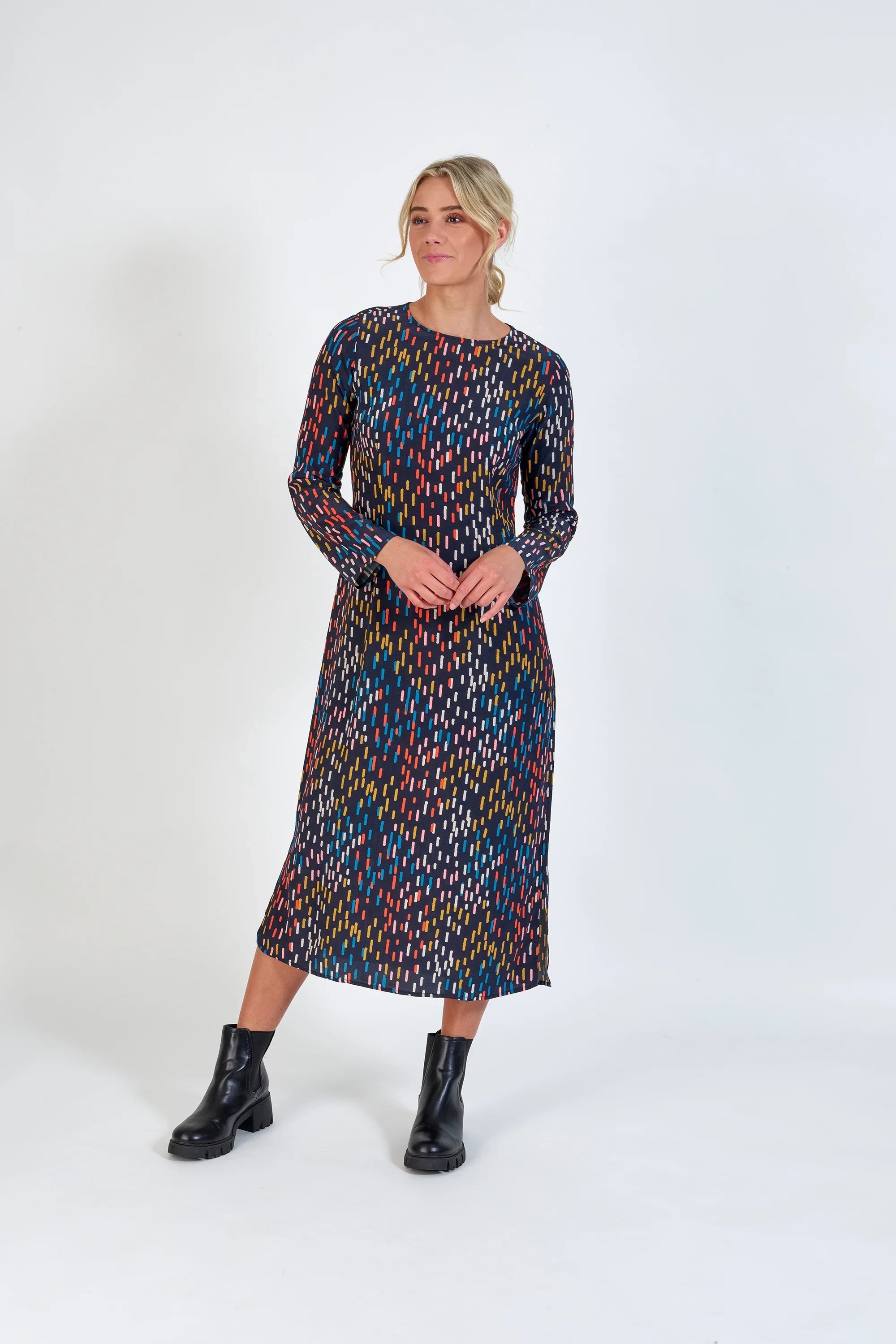 Woman wearing a long-sleeve, midi dress with colorful abstract pattern and black boots