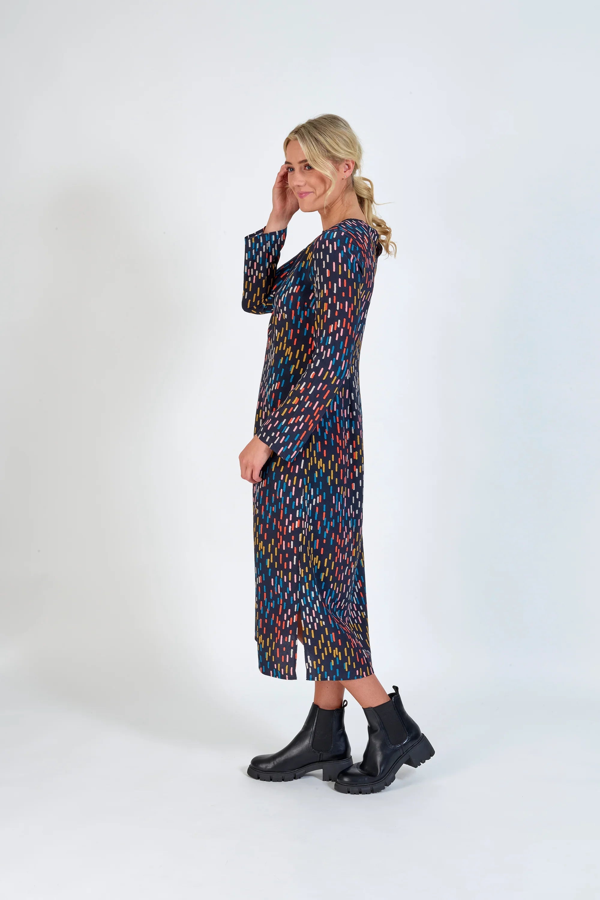 Woman wearing a long-sleeve, multicolour patterned midi dress with black ankle boots, side pose