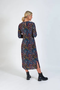 Woman wearing a long sleeve, patterned midi dress with colorful dash print and side slit.