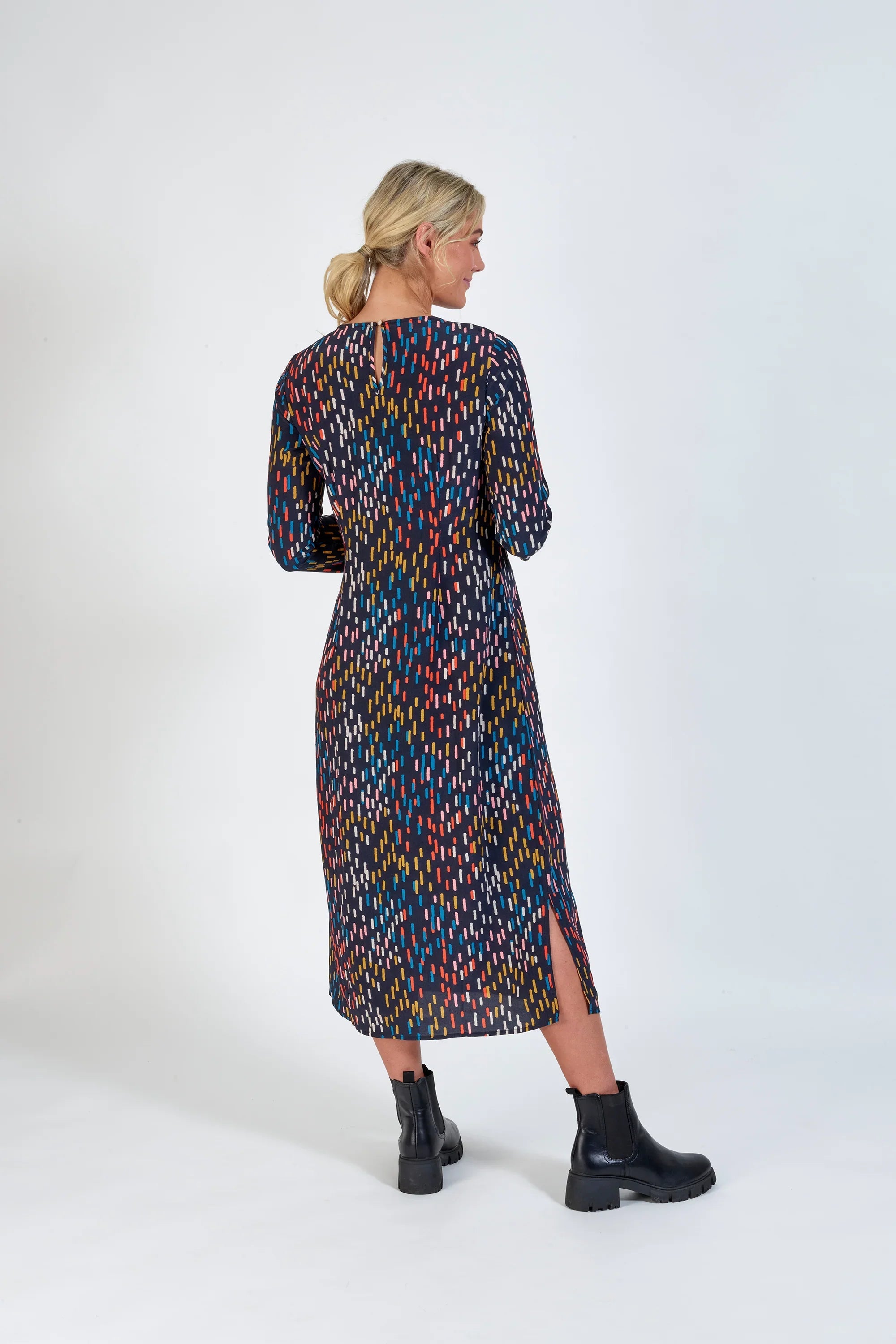 Woman wearing a long sleeve, patterned midi dress with colorful dash print and side slit.