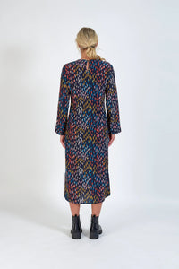 Back view of woman in long sleeve multicolored midi dress and black boots on white background