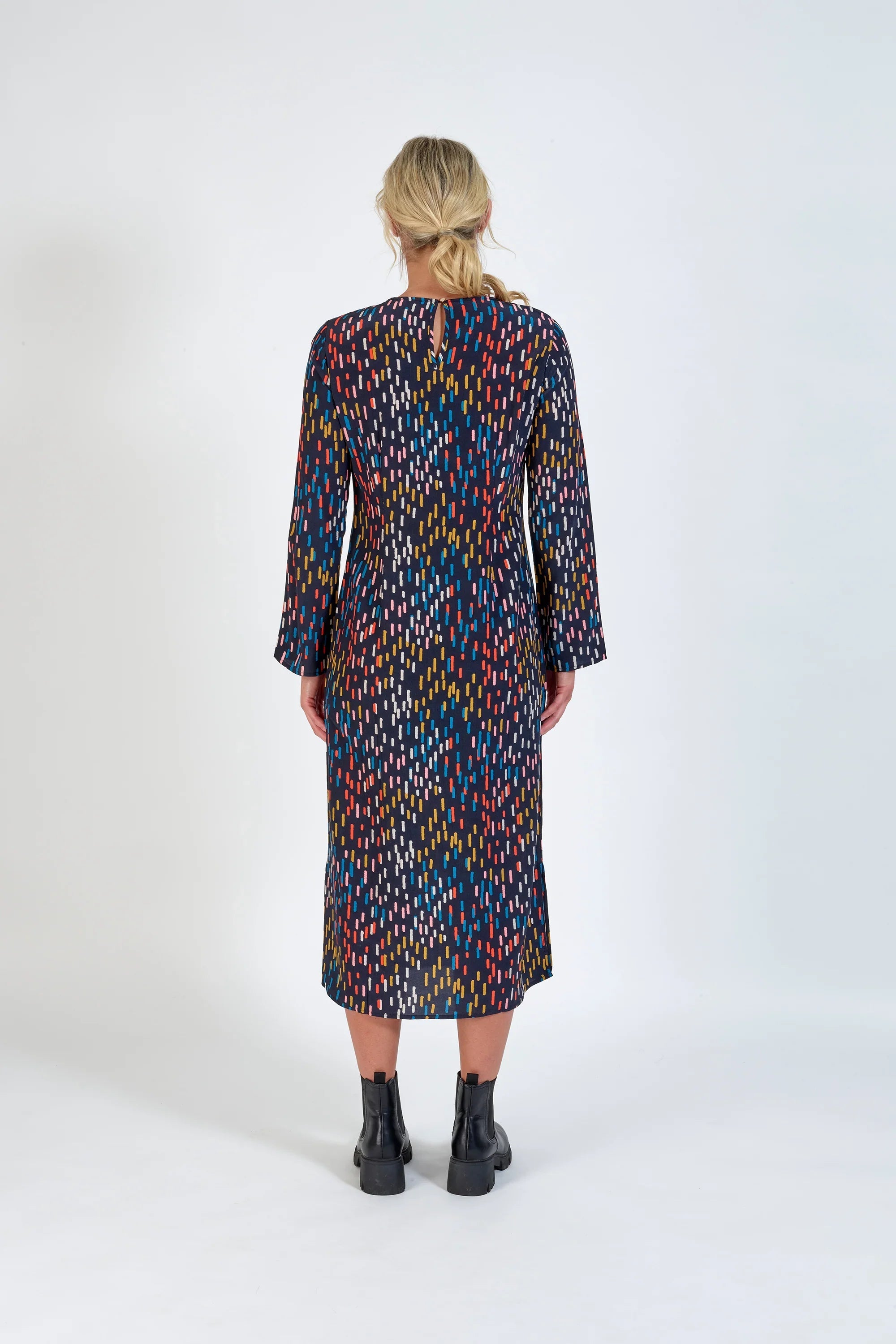 Back view of woman in long sleeve multicolored midi dress and black boots on white background