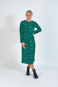 Woman wearing a green geometric long-sleeve midi dress with black ankle boots on a white background.