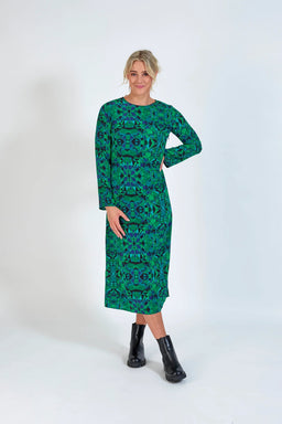 Woman wearing a green geometric long-sleeve midi dress with black ankle boots on a white background.