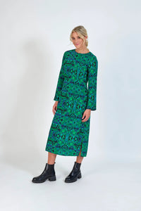 Woman wearing a long sleeve green geometric print midi dress with black ankle boots