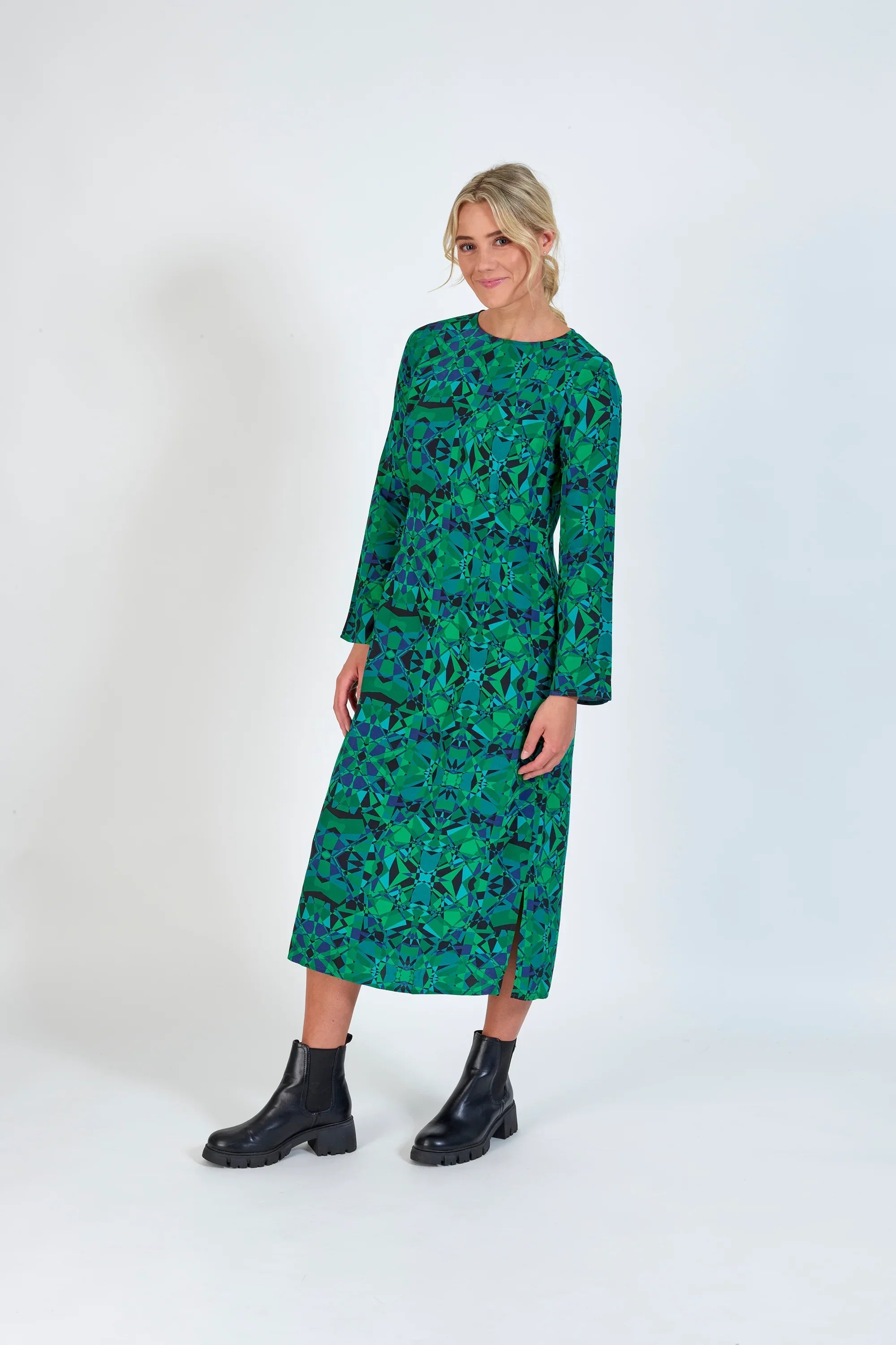 Woman wearing a long sleeve green geometric print midi dress with black ankle boots