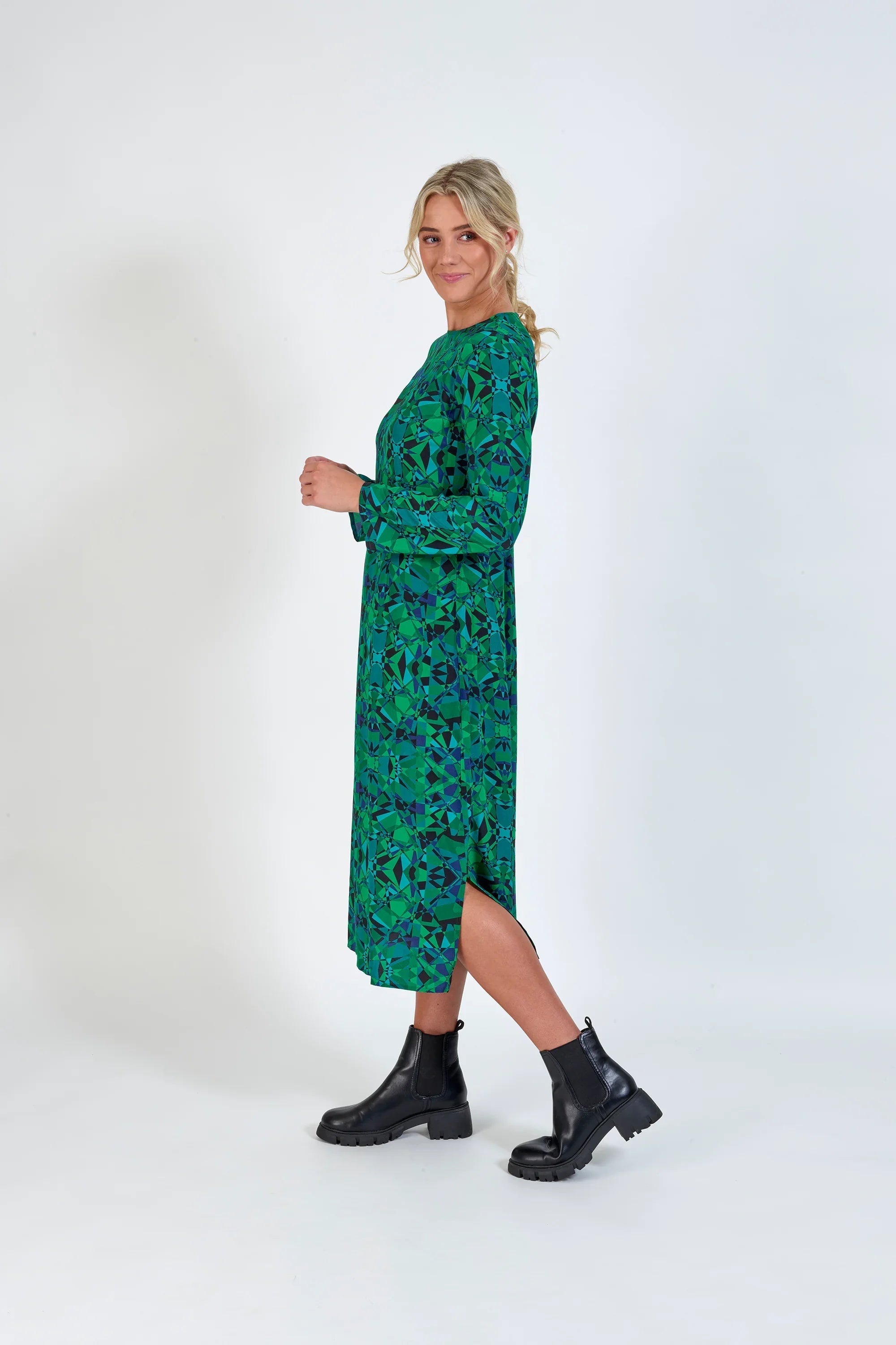 Woman in geometric green long-sleeve midi dress with side slit and black ankle boots